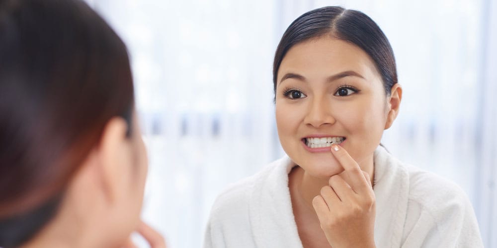 woman looking at her dental work in the mirror in Los Angeles, CA